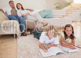 Siblings doing homework on the carpet with parents behind them