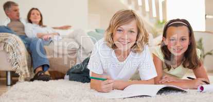 Siblings doing their homework on the floor with parents behind t