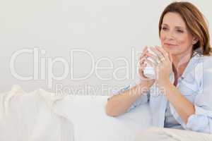 Thoughtful woman with cup of coffee on sofa