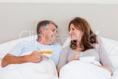 Happy couple eating cereals in bed