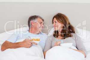 Happy couple eating cereals in bed