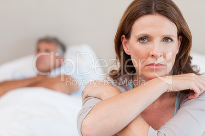 Sad woman on the bed with husband in background