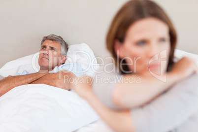 Sad man in bed with his wife in the foreground
