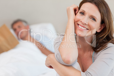 Happy smiling woman on bed with husband reading behind her