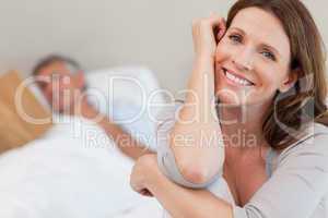 Happy smiling woman on bed with husband reading behind her