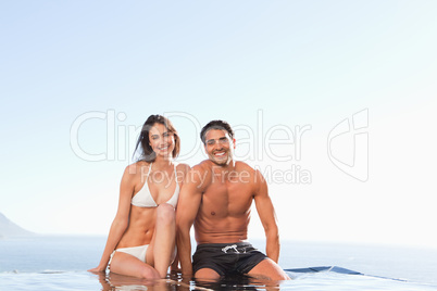 Smiling couple sitting on pool edge