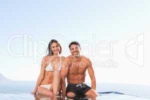Smiling couple sitting on pool edge