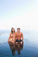 Couple sitting on pool edge with sea in the background
