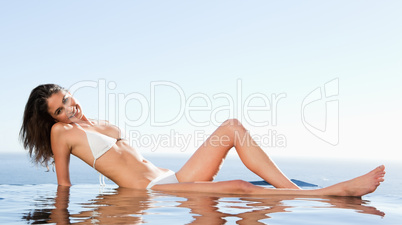 Smiling woman enjoys sunbathing on pool edge