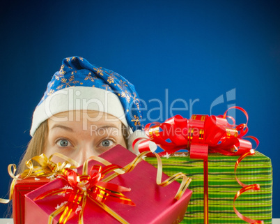 Surprised teen girl looking from behind the Christmas presents