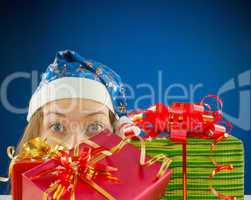 Surprised teen girl looking from behind the Christmas presents