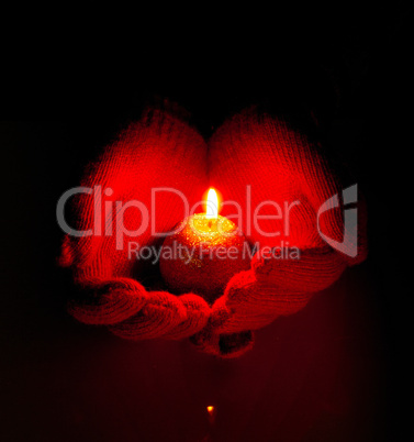 Human hands hold burning candle against dark background