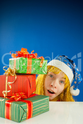 Surprised teen girl looking from behind the Christmas presents