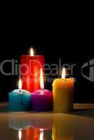 Four colourful burning candles against black background