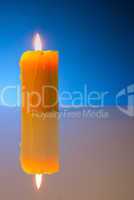 Burning yellow candle against blue background