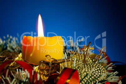 Burning candle with Christmas decorations against blue background