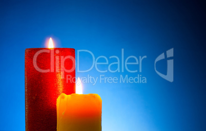 Two burning colourful candles against blue background