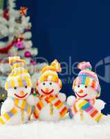 Three snowmen in front of the decorated white evergreen tree ove