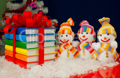 Stack of colorful books tied up with red ribbon and three snowme