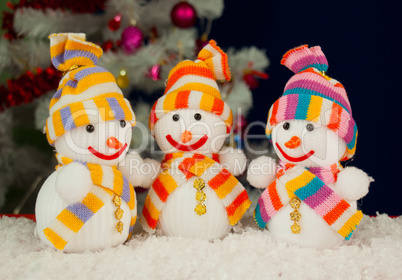 Three snowmen in front of the decorated white evergreen tree ove