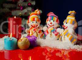 Three snowmen and burning candles over the blue background