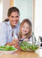 Portrait of a young mother and her daughter preparing a salad