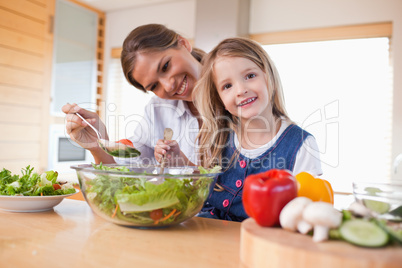 Happy mother and her daughter preparing a salad