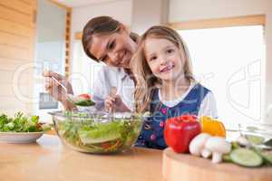 Happy mother and her daughter preparing a salad