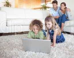 Children using a notebook while their parents are watching