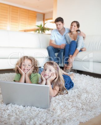 Portrait of cute children using a notebook while their parents a