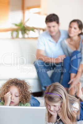 Portrait of children using a laptop while their parents are watc