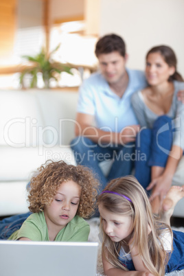 Portrait of young children using a laptop while their parents ar