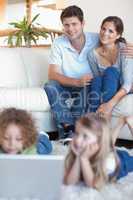 Portrait of parents watching their children using a laptop