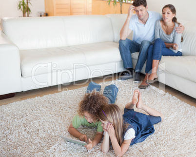 Cute children using a tablet computer while their parents are wa
