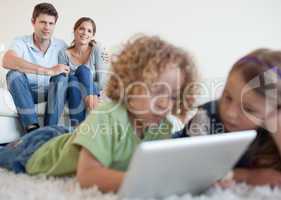 Cute children using a tablet computer while their happy parents
