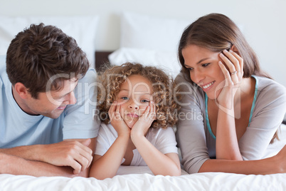 Smiling parents lying on a bed with their son