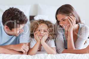 Smiling parents lying on a bed with their son