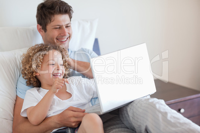 Father and child using laptop in bed