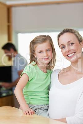 Mother holding her daughter with father in the background