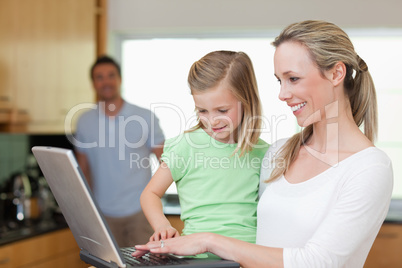 Happy mother and daughter surfing the web with father in the bac