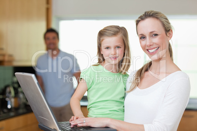 Mother and daughter using laptop with father in the background