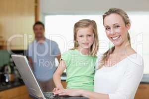 Mother and daughter using laptop with father in the background