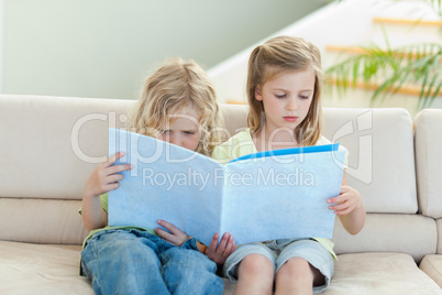 Siblings reading magazine on the sofa
