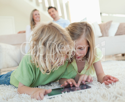 Siblings on the floor with tablet and parents behind them