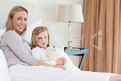 Side view of mother and daughter sitting on the bed