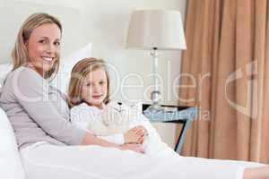 Side view of mother and daughter sitting on the bed