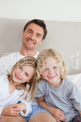 Smiling father sitting on the bed with his children