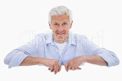 Portrait of a smiling mature man standing behind blank panel