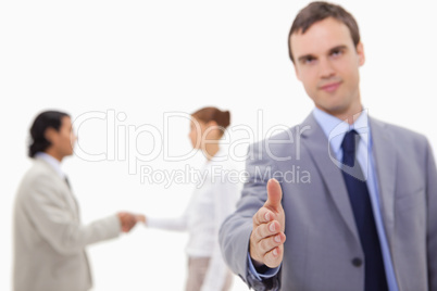 Businessman offering hand with hand shaking colleagues behind hi