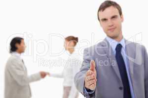 Businessman offering hand with hand shaking colleagues behind hi